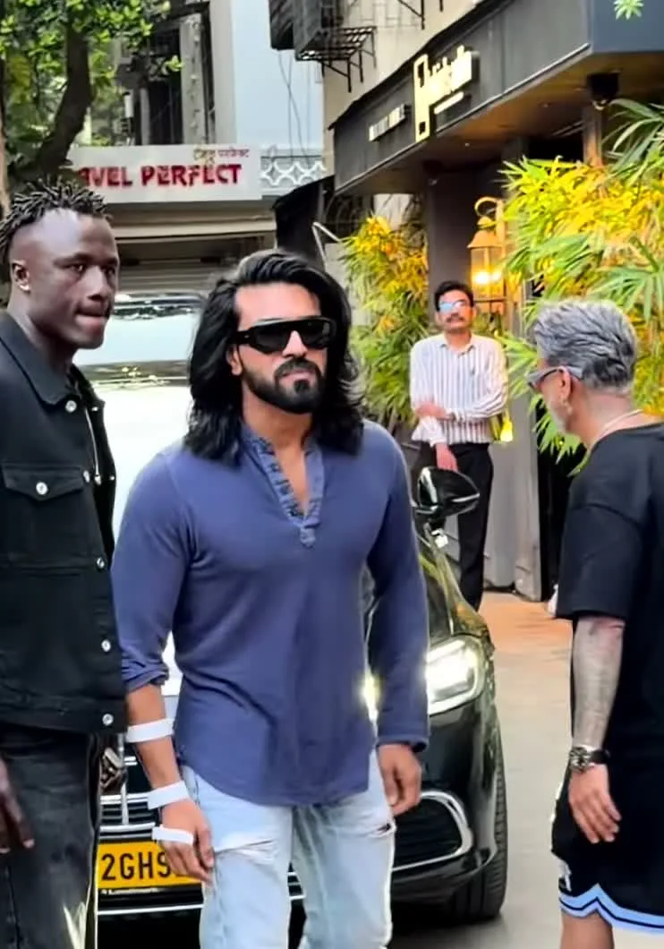 Ram Charan — Mid-step — the sleeves pushed to below the elbow and the knee rips on the jeans