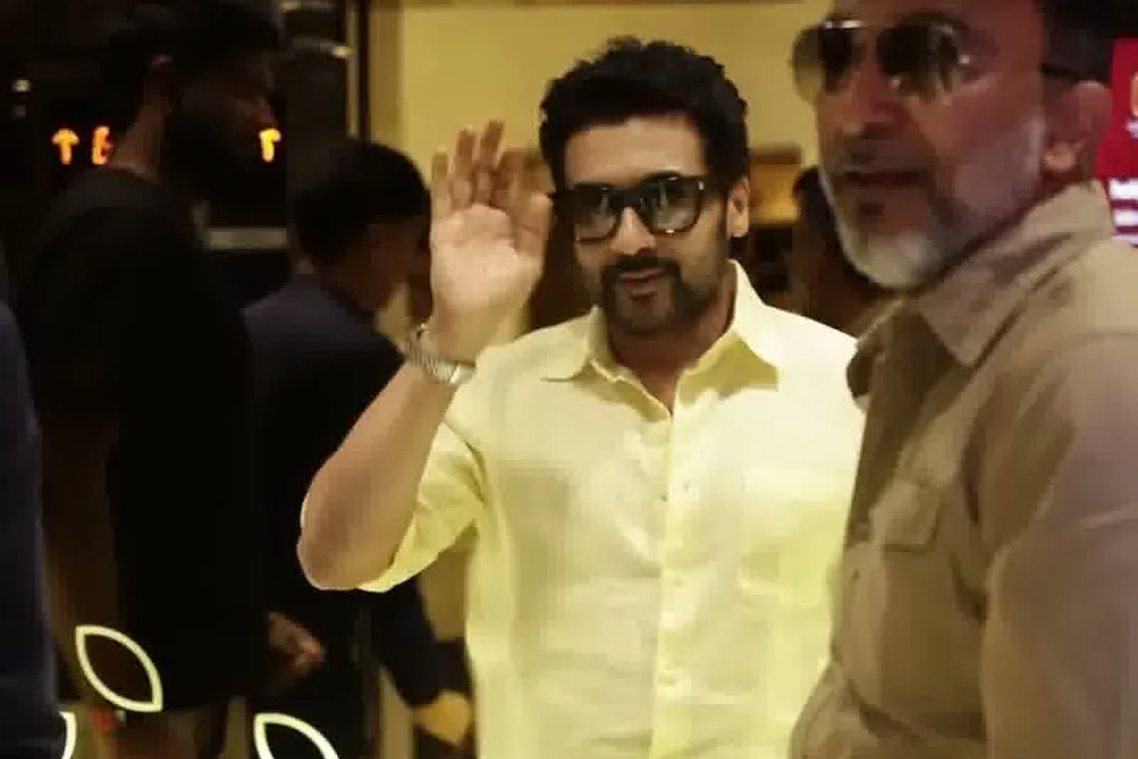 Suriya — Waving inside the mall — the same shirt under warm indoor light, where the yellow reads deeper