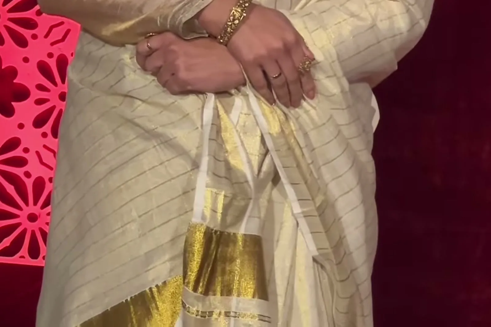 Genelia D’Souza — The hands — stacked gold bangles on the left wrist, rings on both, and the kasavu border where the drape falls