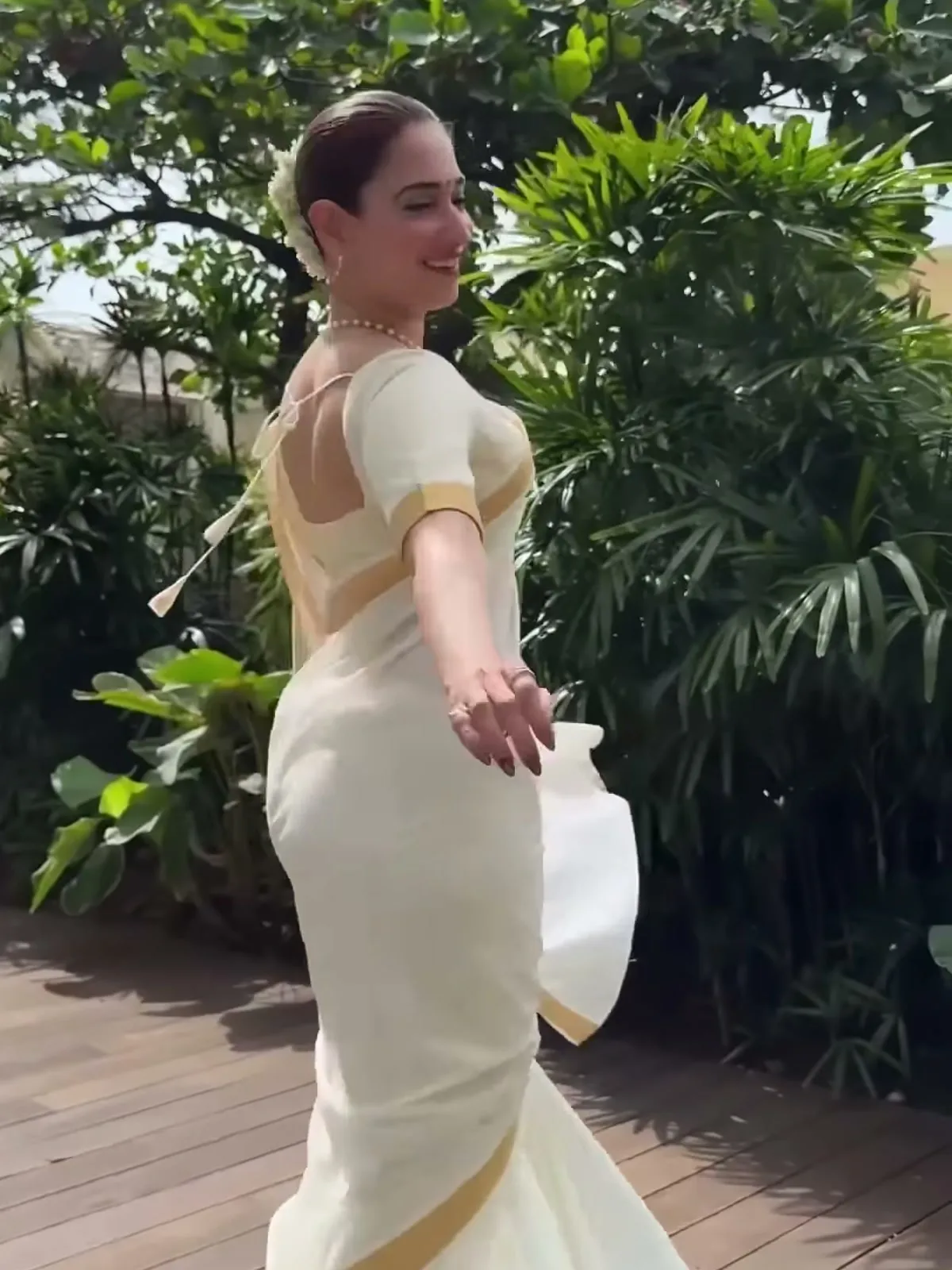 Tamannaah Bhatia — From behind, mid-turn: the deep square back and its plain tie string, the same gold band at the sleeve, and the border running the length of the pallu
